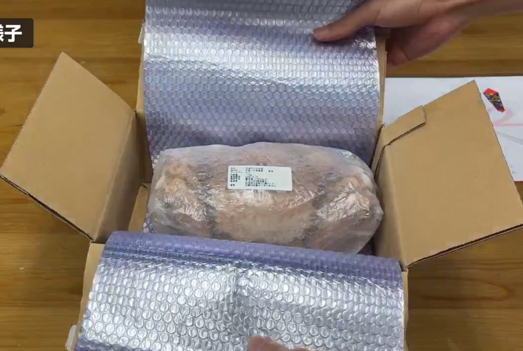 段ボール箱の銀色の保冷材の中央に、包装された冷凍毛ガニが入っている様子
